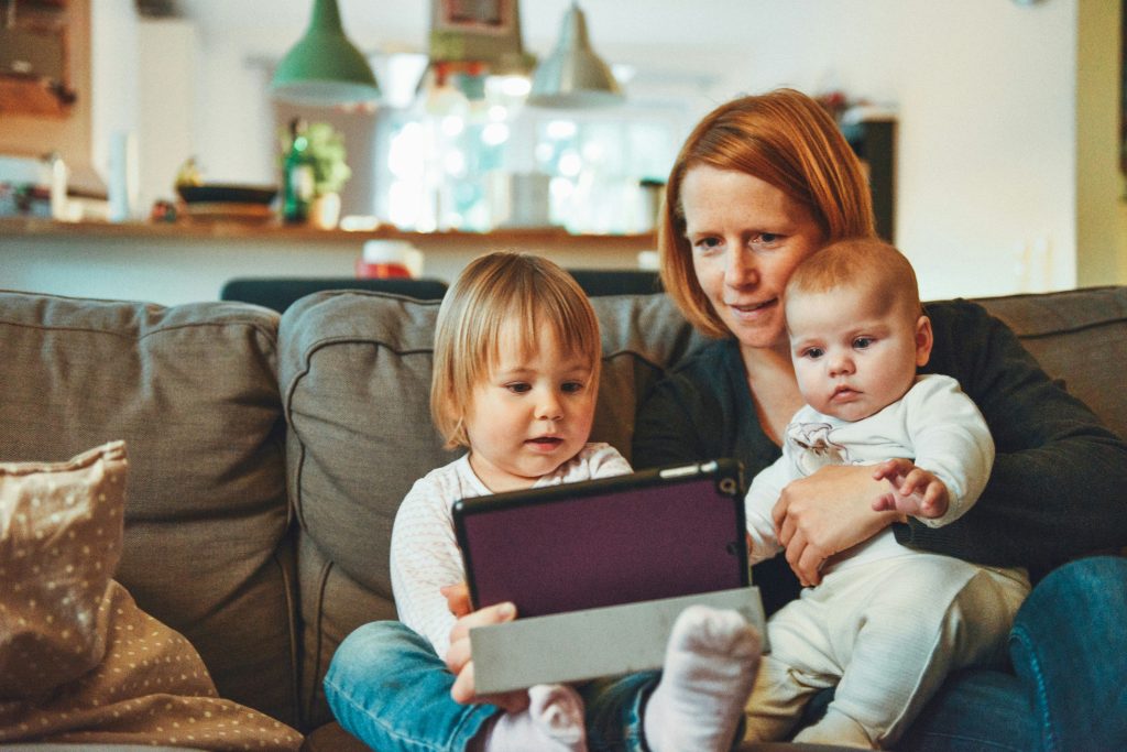 Äiti lasten kanssa sohvalla. Kädessä ipad.