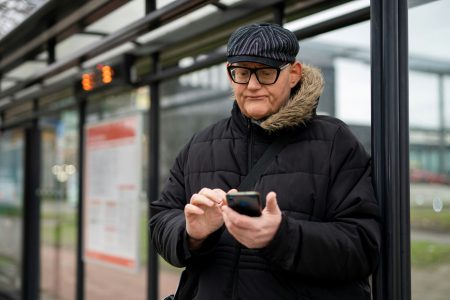Henkilö vastaa kännykällä kyselyyn bussipysäkillä.